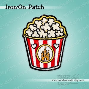 May include: An embroidered iron-on patch featuring a bucket of popcorn with white and red vertical stripes. The bucket displays a central yellow circle containing a brown castle icon, flanked by two small white hearts. The popcorn is white.
