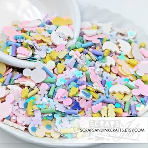 Könnte beinhalten: Eine Auswahl an pastellfarbenen Streuseln, darunter Mickey-Maus-Formen, Sterne und andere lustige Designs. Die Streusel befinden sich in einer weißen Schüssel und sind bereit, zum Dekorieren von Kuchen, Cupcakes oder anderen Leckereien verwendet zu werden.