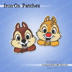 May include: Two embroidered iron-on patches of cartoon chipmunks. One is brown, the other is tan with a red nose. Both have white faces, black eyes, and are smiling. The text "Iron-On Patches" is at the top.