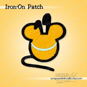Op de afbeelding: Een opstrijkbare patch met een gele muisvorm, zwarte contouren en een zwarte staart. De muis heeft een lichtblauwe streep. De tekst "Iron-On Patch" staat bovenaan. Voor decoratieve doeleinden.