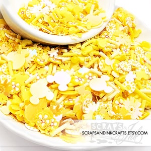 Puede incluir: Un bol de espolvorear amarillo y blanco con varias formas, incluyendo cabezas de Mickey Mouse, flores y estrellas. Los espolvorear son perfectos para decorar pasteles, cupcakes y otros postres.