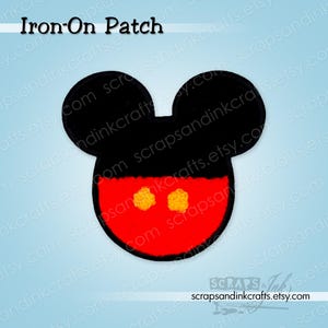 Könnte beinhalten: Schwarzer Aufnäher in Form von Mickey Mouses Kopf. Der Aufnäher hat schwarze Ohren, ein rotes Gesicht und zwei gelbe, gestickte Knöpfe. Der Text "Iron-On Patch" steht oben.