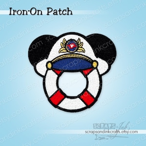May include: An embroidered iron-on patch featuring a white and red life preserver ring topped with a white captain's hat. The hat has a blue brim, gold accents, and a central emblem. Two black rounded ears are positioned behind the hat.