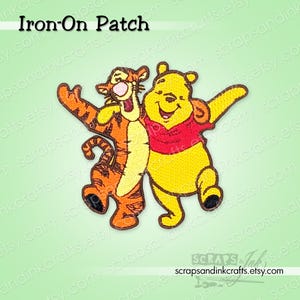 May include: An embroidered iron-on patch featuring the characters Tigger and Winnie the Pooh standing side by side. Tigger is orange with black stripes, and Winnie the Pooh is yellow wearing a red shirt. The text Iron-On Patch is at the top.