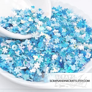 May include: A bowl filled with blue and white glitter, featuring snowflake, Mickey Mouse, and other shapes. The glitter is perfect for crafting and adding sparkle to projects.