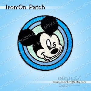 Può includere: Toppa rotonda da stirare con il volto di Topolino. La toppa presenta un volto in bianco e nero con un'espressione sorridente, incastonato su uno sfondo circolare blu e azzurro. Il testo "Iron-On Patch" è in alto.
