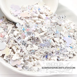 May include: White, iridescent, and clear sprinkles in a variety of shapes, including stars, Mickey Mouse heads, and clouds. The sprinkles are in a white bowl and are ready to be used for decorating.
