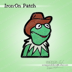 May include: Embroidered iron-on patch featuring Kermit the Frog wearing a brown cowboy hat. The patch has a green frog with a white collar and a red mouth. The text "Iron-On Patch" is at the top.