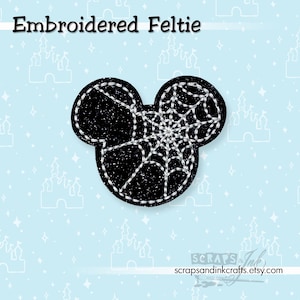 May include: Black embroidered feltie in the shape of a mouse head with a spiderweb design. The feltie has white stitching and is on a light blue background with castle and star patterns. The text "Embroidered Feltie" is at the top.