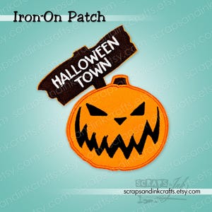 Puede incluir: Un parche termoadhesivo bordado de color naranja con una calabaza de Halloween con boca dentada y ojos triangulares. Un letrero marrón en la parte superior dice "HALLOWEEN TOWN" en letras blancas. Un artículo de manualidades con temática de Halloween.