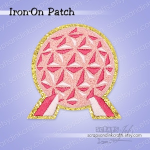 May include: Embroidered iron-on patch featuring a pink and white geometric design within a gold glitter border. The patch has a rounded shape with two supporting structures at the bottom. Text at the top reads "Iron-On Patch".