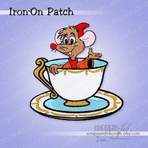 May include: Embroidered iron-on patch featuring a cartoon mouse character in an orange outfit and red hat, sitting in a white teacup with gold trim. The teacup rests on a blue saucer with gold detailing. Text at the top reads "Iron-On Patch".