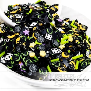 May include: A selection of Halloween-themed sprinkles in black, green, yellow and white. The sprinkles include spiders, bats, ghosts and dice.