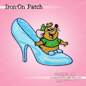 May include: Embroidered iron-on patch featuring a cartoon mouse character inside a blue glass slipper. The mouse wears a green shirt and a matching hat. The text "Iron-On Patch" is at the top.