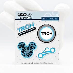Può includere: Un set di quattro adesivi a tema Tron che mostrano una testa di Topolino blu e nera, una moto di luce blu e nera, un logo Tron blu e nero e un logo Tron blu e nero con il testo "LIGHTCYCLE/RUN".