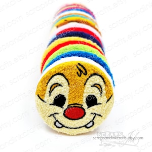 May include: A stack of colourful, round, plush fabric circles with a cartoon character's face embroidered on the front. The character has a yellow face, brown ears, and a red nose. The character is smiling with white teeth.