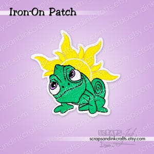 Könnte beinhalten: Ein Bügelbild mit Pascal, dem grünen Chamäleon aus dem Film Rapunzel, mit einem gelben Sonnendesign im Hintergrund. Der Aufnäher hat einen weißen Rand und den Text "Iron-On Patch" oben.