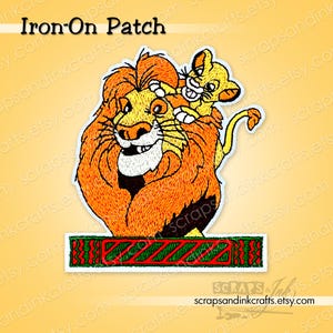 May include: Embroidered iron-on patch depicting a lion and cub. The lion has an orange mane and the cub is yellow. The patch includes the text "Iron-On Patch" at the top and a decorative green and red border at the bottom.