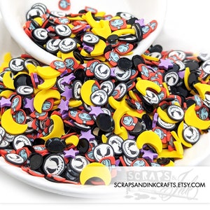 Puede incluir: Una variedad de encantos de resina coloridos en forma de lunas, estrellas y la cara de Jack Skellington. Los encantos están esparcidos sobre una superficie blanca.