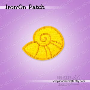 May include: A yellow embroidered iron-on patch in the shape of a spiral seashell. The patch features a central spiral design with radiating lines and a thick border. The text Iron-On Patch is visible at the top, and the URL scrapsandinkcrafts.etsy.com is at the bottom.