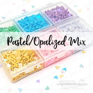 May include: A clear plastic container with six compartments, each filled with pastel-colored, opalescent confetti. The confetti is shaped like small hearts and Mickey Mouse heads. The text "Pastel/Opalized Mix" is overlaid on the image.
