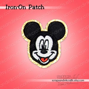 May include: Iron-on patch featuring Mickey Mouse's face. The patch has a black head and ears, a white face, and a red tongue. The border is gold glitter. The text "Iron-On Patch" is at the top.