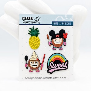 Peut inclure: Une carte avec quatre épingles en émail aux motifs de dessins animés. Les épingles représentent un ananas jaune, un personnage de noix de coco avec un pinceau, un personnage de crème glacée à la noix de coco avec une cuillère et un arc-en-ciel avec le mot "Sweet". La carte porte les textes "Scraps & Ink" et "Bits & Pieces".