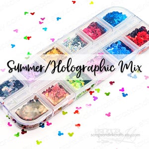 May include: A clear plastic container filled with various colors of holographic sequins in a variety of shapes. The container is labeled "Summer/Holographic Mix". Scattered around the container are small, colorful Mickey Mouse head-shaped sequins.