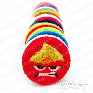 May include: A stack of colorful felt circles with embroidered faces. The top circle is red with a yellow triangle and an angry expression.