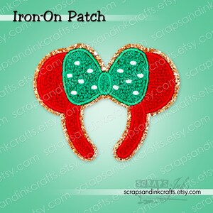 May include: An iron-on patch shaped like mouse ears with a red base and a green bow featuring white polka dots. The entire edge of the patch is outlined with a shimmering gold glitter border. The text Iron-On Patch is visible at the top.