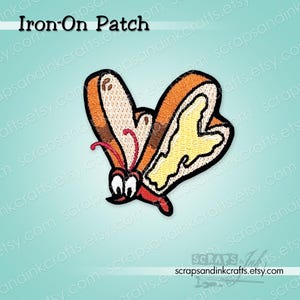 May include: An embroidered iron-on patch featuring a whimsical butterfly shaped like a slice of toast with a yellow butter spread. The design includes brown crust edges, white bread centres, and two small white eyes with black pupils and red antennae.