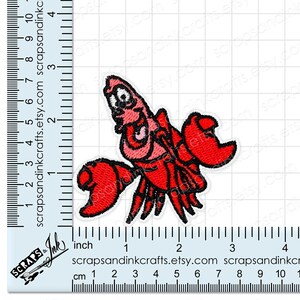 May include: Embroidered patch featuring a cartoon lobster in shades of red and pink with black outlines. The patch is approximately 2 inches wide and 2 inches tall. The patch is on a white background.