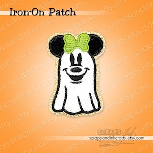 May include: An embroidered iron-on patch featuring a white ghost character with black ears and a bright lime green bow. The design has a gold glitter border and the text Iron-On Patch is visible at the top of the image against an orange background.