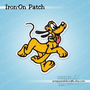 Puede incluir: Un parche bordado termoadhesivo que muestra un perro de dibujos animados amarillo con orejas negras, un collar verde y una lengua rosa, en una pose juguetona. El texto Iron-On Patch y el nombre del sitio web son visibles en la imagen.