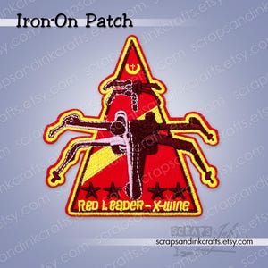 Könnte beinhalten: Aufbügler mit einem roten, gelben und schwarzen X-Wing-Jäger-Design. Der Aufnäher enthält den Text "Red Leader - X-wing" und drei Sterne. Der Aufnäher ist mit gelben Nähten eingefasst.