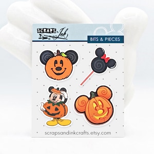 以下が含まれることがあります： ミッキーマウス風のパンプキンデザインとロリポップが特徴のハロウィーンをテーマにしたステッカーシート。ステッカーはオレンジ、黒、白で、「SCRAPS & Ink」と「BITS & PIECES」の文字が入っています。「scrapsandinkcrafts.etsy.com」のウェブサイトアドレスも表示されています。