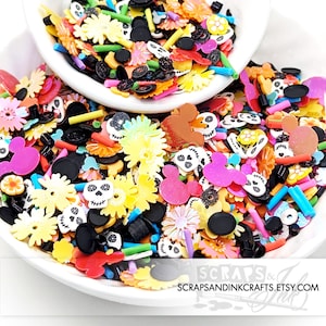 May include: A bowl filled with colorful resin charms, including skulls, flowers, Mickey Mouse ears, and black and white sprinkles. The charms are perfect for adding a fun and whimsical touch to crafts and projects.
