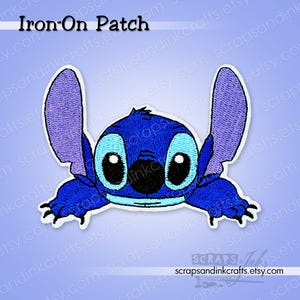 May include: An embroidered iron-on patch of the character Stitch from Lilo & Stitch. The patch is predominantly blue with purple ears and black details. The text "Iron-On Patch" is displayed at the top of the patch.