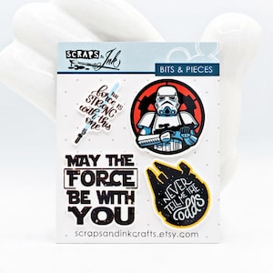 Könnte beinhalten: Vier Star Wars-Sticker auf weißem Hintergrund. Die Sticker zeigen einen Stormtrooper, einen TIE-Jäger, ein Lichtschwert und den Text "Möge die Macht mit dir sein". Der Text "Sag mir nie die Chancen" befindet sich auf dem TIE-Jäger-Sticker. Der Text "Die Macht ist stark mit diesem hier" befindet sich auf dem Lichtschwert-Sticker. Der Text "Scraps & Ink Bits & Pieces" befindet sich oben auf dem Blatt.