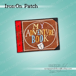 May include: A rectangular iron-on patch featuring a brown book cover design with a red spine and black corners. The text MY ADVENTURE BOOK is embroidered in white, yellow, and blue, with a small white globe icon at the bottom centre.