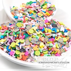 May include: A colorful mix of cake, star, and squiggle shaped sprinkles. The sprinkles are in a white bowl and are ready to be used for decorating.