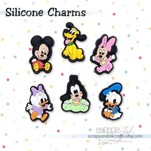 May include: Silicone charms featuring cartoon characters Mickey Mouse, Pluto, Minnie Mouse, Daisy Duck, Goofy, and Donald Duck. The charms are colorful, with black outlines and various colors like yellow, pink, purple, and blue. The text "Silicone Charms" is at the top.