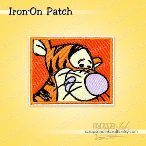 Può includere: Toppa termoadesiva arancione e bianca con un personaggio dei cartoni animati, una tigre e un orso che si abbracciano. La toppa ha una forma rettangolare con un bordo bianco. Il testo "Iron-On Patch" è in alto. Per decorare vestiti e accessori.