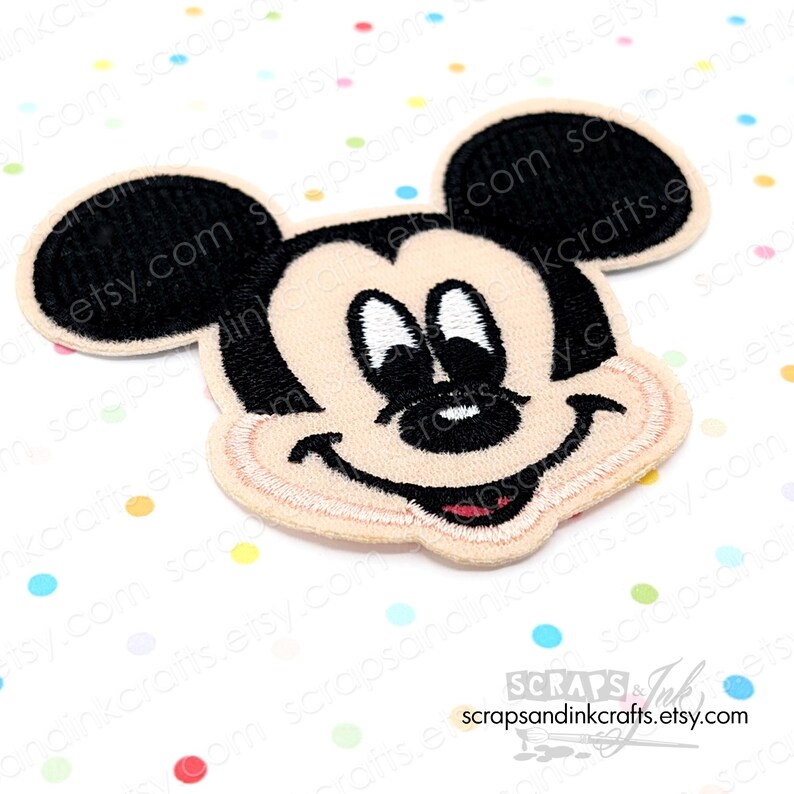 Pode incluir: Patch bordado com o rosto do Mickey Mouse. O patch tem um rosto bege, orelhas pretas e uma express&atilde;o sorridente com a boca vermelha. O patch &eacute; cercado por uma borda bege. O texto "scrapsandinkcrafts.etsy.com" est&aacute; na parte inferior.