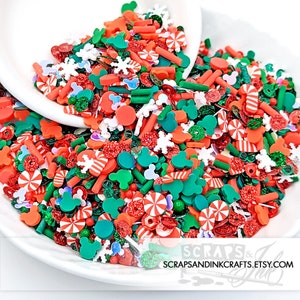 May include: A white bowl filled with colorful Christmas-themed sprinkles. The sprinkles are in the shape of candy canes, snowflakes, Mickey Mouse heads, and other festive designs. The sprinkles are red, green, white, and orange.