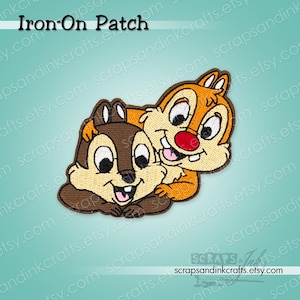 May include: An embroidered iron-on patch featuring two cartoon chipmunks. One chipmunk is dark brown with a light tan face, while the other is light orange with a tan face and a bright red nose. Both have white eyes and visible teeth.