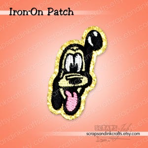 Può includere: Una toppa termoadesiva raffigurante un cane dei cartoni animati con corpo nero, occhi bianchi e lingua rosa. La toppa è bordata di glitter dorati e presenta la scritta "Iron-On Patch" in alto. Lo sfondo è un gradiente di arancione e rosa.