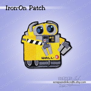 May include: Yellow iron-on patch featuring the WALL-E robot character. The patch has a black border and includes the robot's eyes, arms, and treads. The text "WALL-E" is visible on the patch.