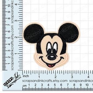 Pode incluir: Patch bordado com o rosto do Mickey Mouse. O patch tem um fundo bege com orelhas e contornos pretos. O rosto inclui olhos brancos, um nariz preto e uma boca vermelha. O patch mede aproximadamente 7.6 cm de altura.