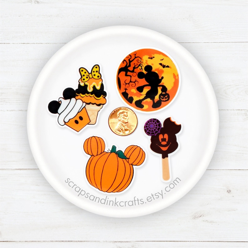 Pu&ograve; includere: Cinque adesivi di personaggi Disney a tema Halloween su un piatto bianco. Gli adesivi raffigurano Topolino, Minnie Mouse, una zucca, un gelato al cioccolato Mickey Mouse e un cono gelato Mickey Mouse.